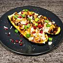 Mit Hackfleisch gefüllte Zucchini, garniert mit Parmesanhobeln, Granatapfelkernen und grünen Frühlingszwiebelringen.