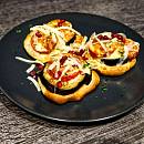 Mini Pizza belegt mit Aubergine und Tomate und mit frisch geriebenem Käse bestreut. Als Farbklecks ein paar Granatapfelkerne.