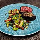 Ein medium-rare gebratenes Rinderfilet liegt aufgeschnitten auf einem Teller, dabei knackiges gemischtes Gemüse.