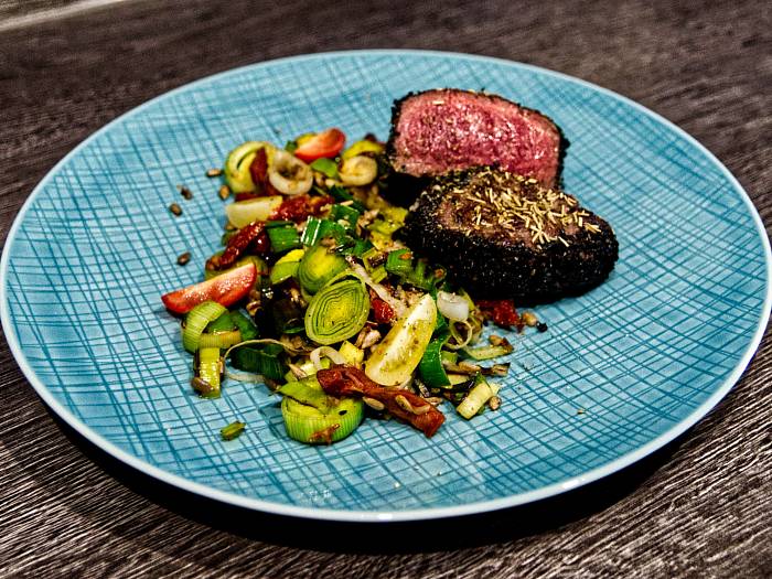 Ein medium-rare gebratenes Rinderfilet liegt aufgeschnitten auf einem Teller, dabei knackiges gemischtes Gemüse.