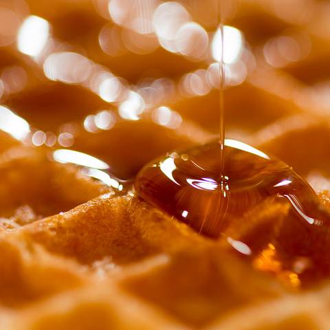 Detailaufnahme einer Waffel, auf die Ahornsirup tropft.
