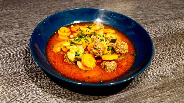 Gemüsesuppe mit Hackbällchen in dunkelblauem Teller