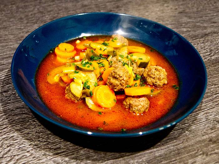 Gemüsesuppe mit Hackbällchen in dunkelblauem Teller