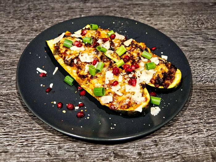 Mit Hackfleisch gefüllte Zucchini, garniert mit Parmesanhobeln, Granatapfelkernen und grünen Frühlingszwiebelringen.