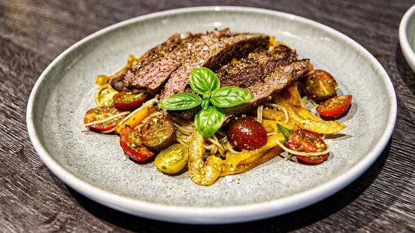 Steakstreifen auf dünnen Spaghetti mit gelben Paprikastreifen und bunten, halbierten Cocktailtomaten, garniert mit frischem Basilikum.