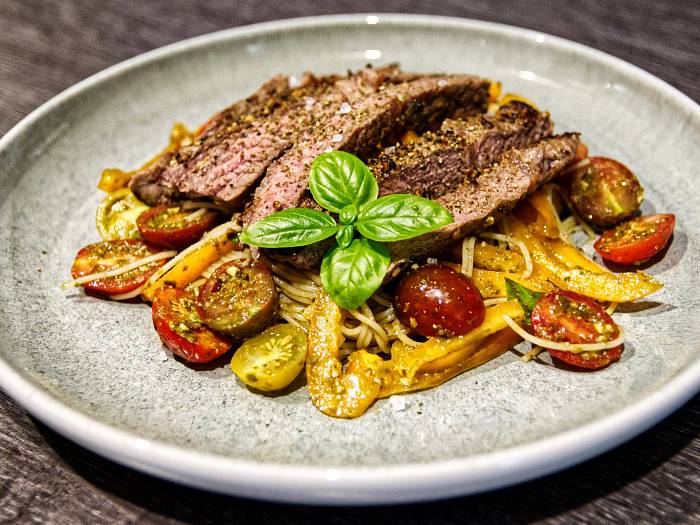 Steakstreifen auf dünnen Spaghetti mit gelben Paprikastreifen und bunten, halbierten Cocktailtomaten, garniert mit frischem Basilikum.