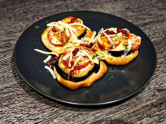 Mini Pizza belegt mit Aubergine und Tomate und mit frisch geriebenem Käse bestreut. Als Farbklecks ein paar Granatapfelkerne.