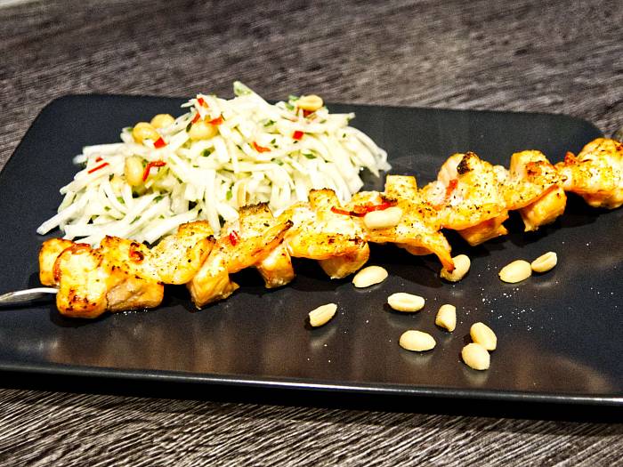 Spieß mit Lachs und Garnelen neben einem Salat aus Kohlrabi