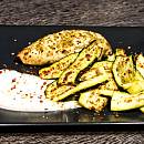 Gebratene Hähnchenbrust an gebratenen Zucchini auf einem schwarzen Teller mit weißem Dip im Vordergrund