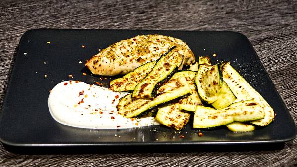 Gebratene Hähnchenbrust an gebratenen Zucchini auf einem schwarzen Teller mit weißem Dip im Vordergrund
