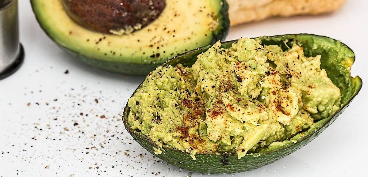Aufgeschnittene Avocado im Hintergrund und im Vordergrund eine Guacamole in der Avocadoschale.