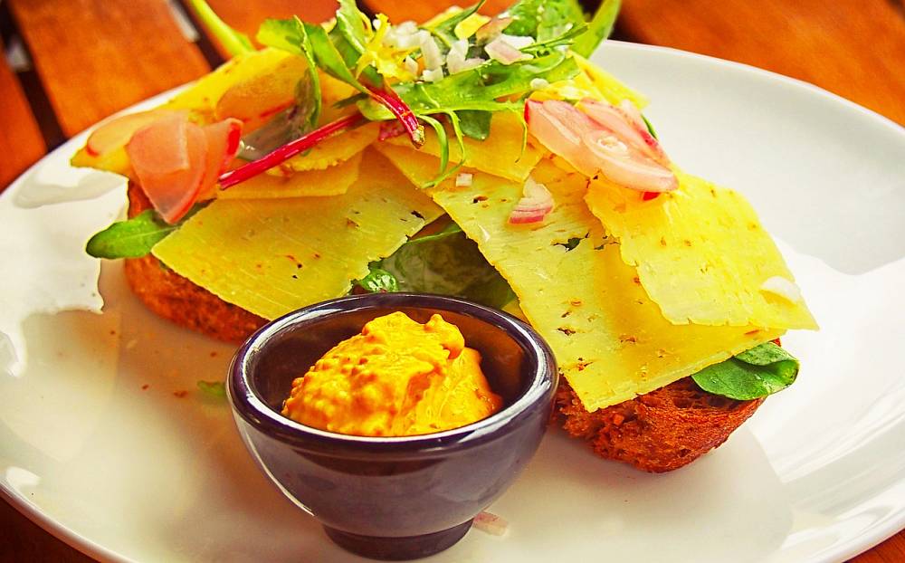 Ein belegtes Brot. Im Vordergrund steht ein kleines Schüsselchen mit Senf.