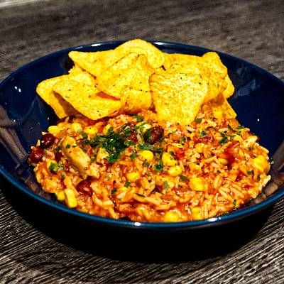 One-Pot-Reis-Topf in einem dunklen Teller, dazu liegen Tortilla-Chips dabei.
