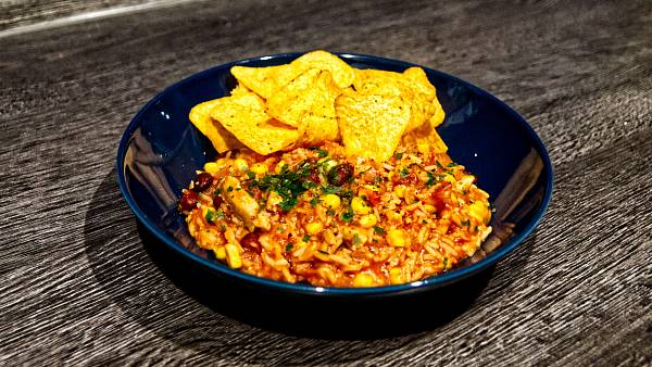 One-Pot-Reis-Topf in einem dunklen Teller, dazu liegen Tortilla-Chips dabei.