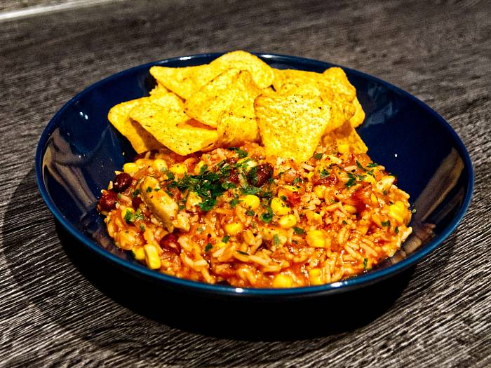 One-Pot-Reis-Topf in einem dunklen Teller, dazu liegen Tortilla-Chips dabei.