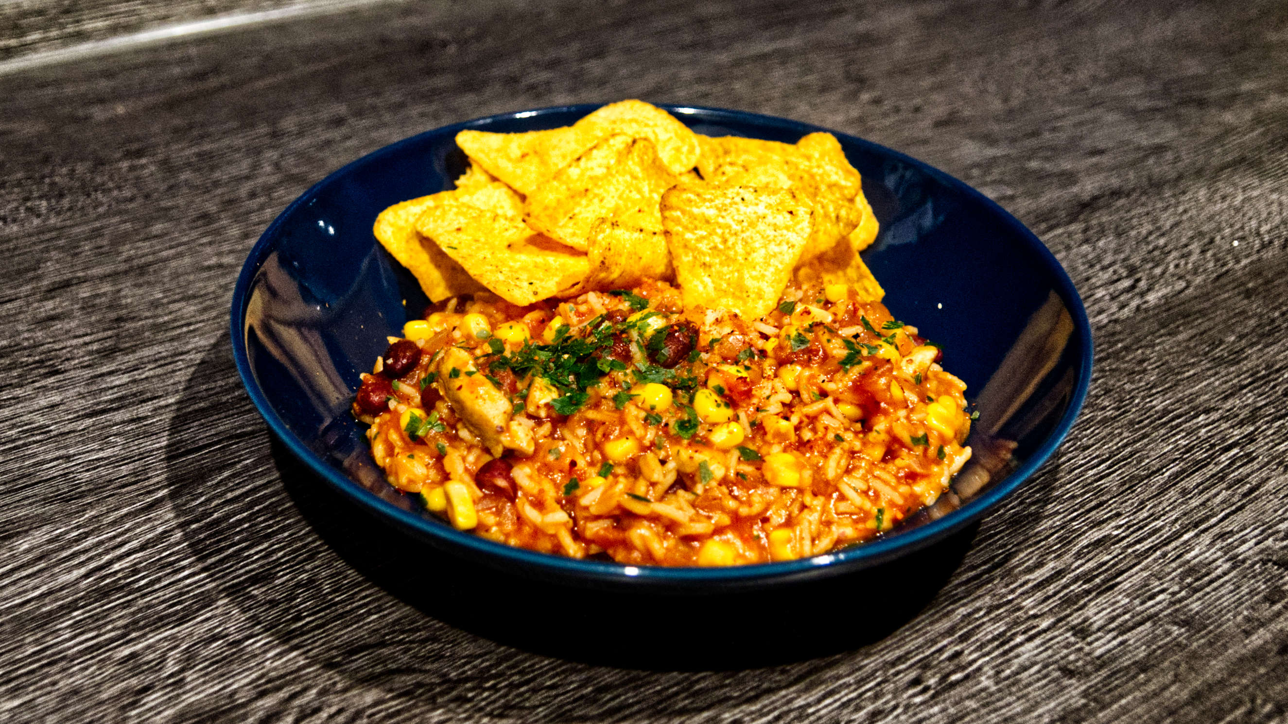 One-Pot-Reis-Topf in einem dunklen Teller, dazu liegen Tortilla-Chips dabei.