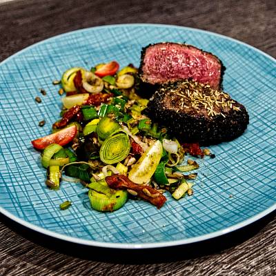 Ein medium-rare gebratenes Rinderfilet liegt aufgeschnitten auf einem Teller, dabei knackiges gemischtes Gemüse.