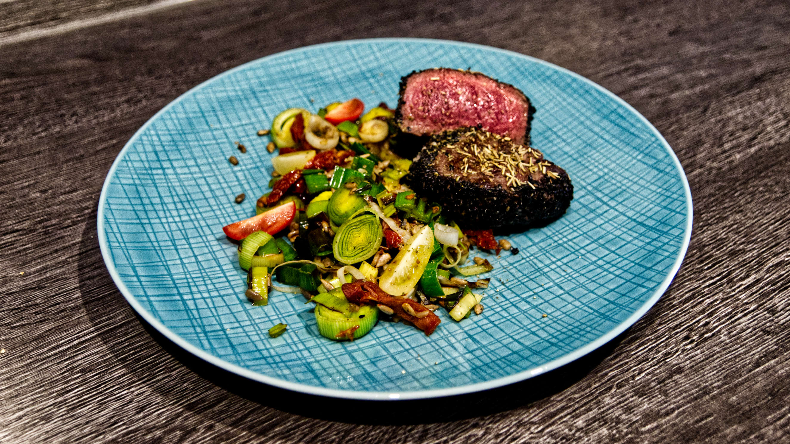 Ein medium-rare gebratenes Rinderfilet liegt aufgeschnitten auf einem Teller, dabei knackiges gemischtes Gemüse.