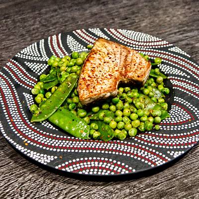 Ein gebratenes Thunfisch-Steak liegt auf leuchtend grünen Erbsen und Zuckerschoten.
