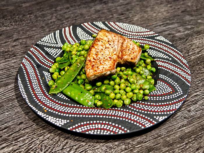 Ein gebratenes Thunfisch-Steak liegt auf leuchtend grünen Erbsen und Zuckerschoten.