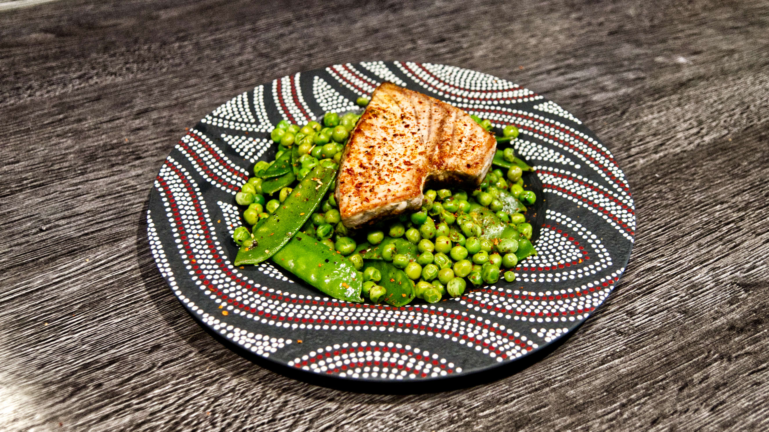 Ein gebratenes Thunfisch-Steak liegt auf leuchtend grünen Erbsen und Zuckerschoten.