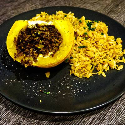 Ein halber kleiner Mikrowellenkürbis mit Hackfüllung neben gebratenem Reis.