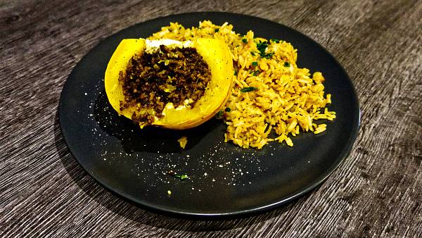 Ein halber kleiner Mikrowellenkürbis mit Hackfüllung neben gebratenem Reis.