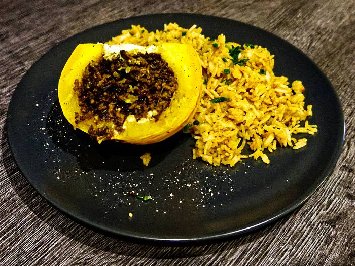 Ein halber kleiner Mikrowellenkürbis mit Hackfüllung neben gebratenem Reis.